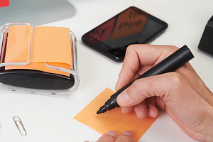 a man prepares to write a task note at a desk, a Photo by Nito