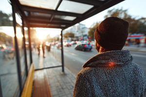 A man waits at a bus stop during sunset, wearing a warm beanie and a stylish co, a Person Photo by ImageMir