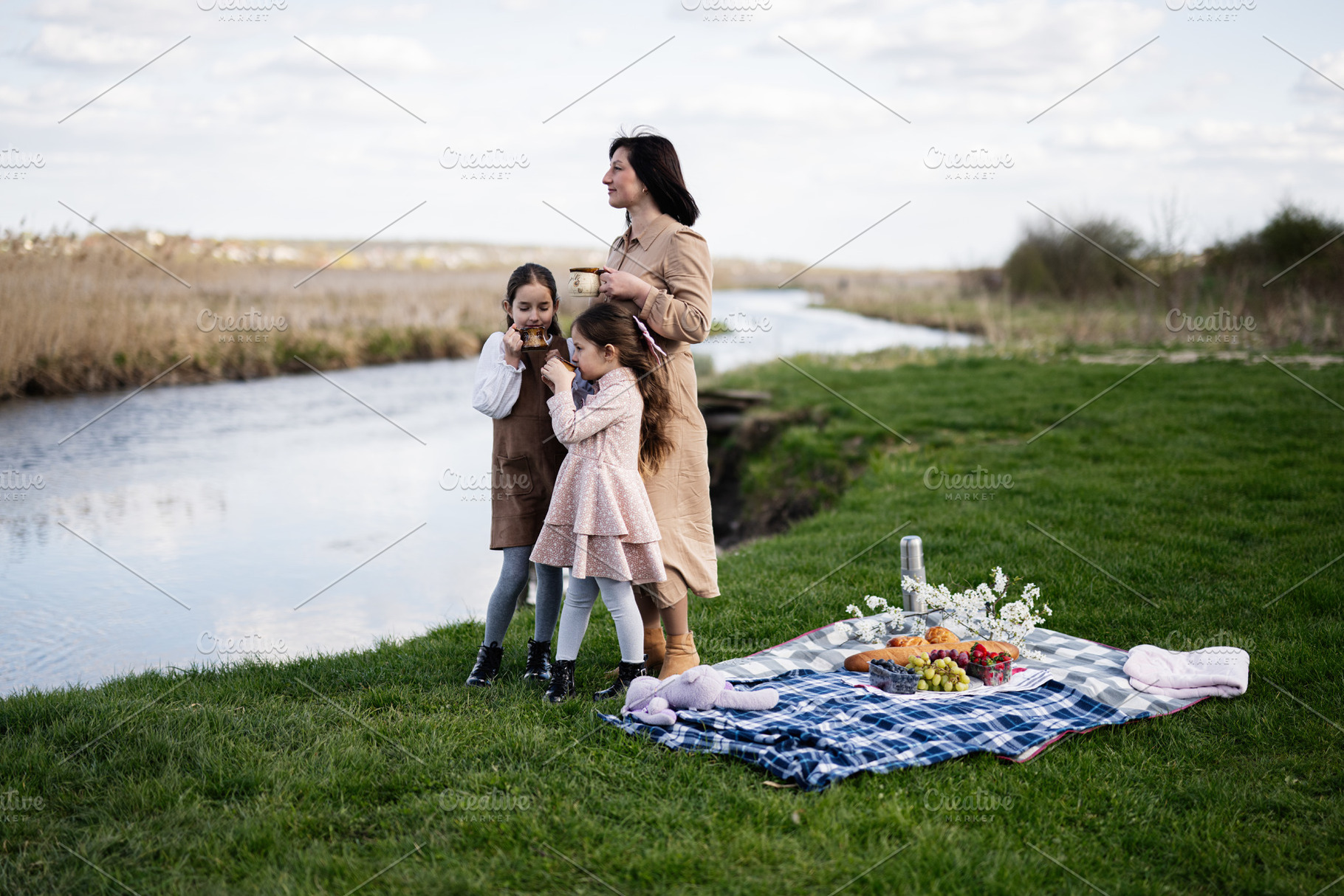 Mother and daughters enjoying a riverside picnic together on a blanket with foo, a Person Photo by AS photostudio
