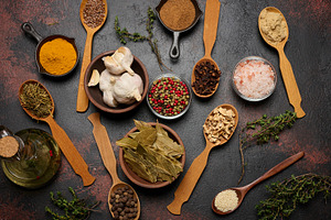 Various ground spices in wooden spoons, olive oil on dark table, a Food & Drink Photo by ndanko