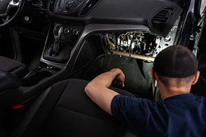 Mechanic inspecting under dashboard wiring inside a car interior, a Transportation Photo by AS photostudio