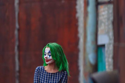 Portrait of a greenhaired girl in chekered dress with joker makeup on a rusty m