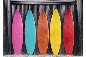 Colored surfboards leaning up against a wooden fence featuring surfboard