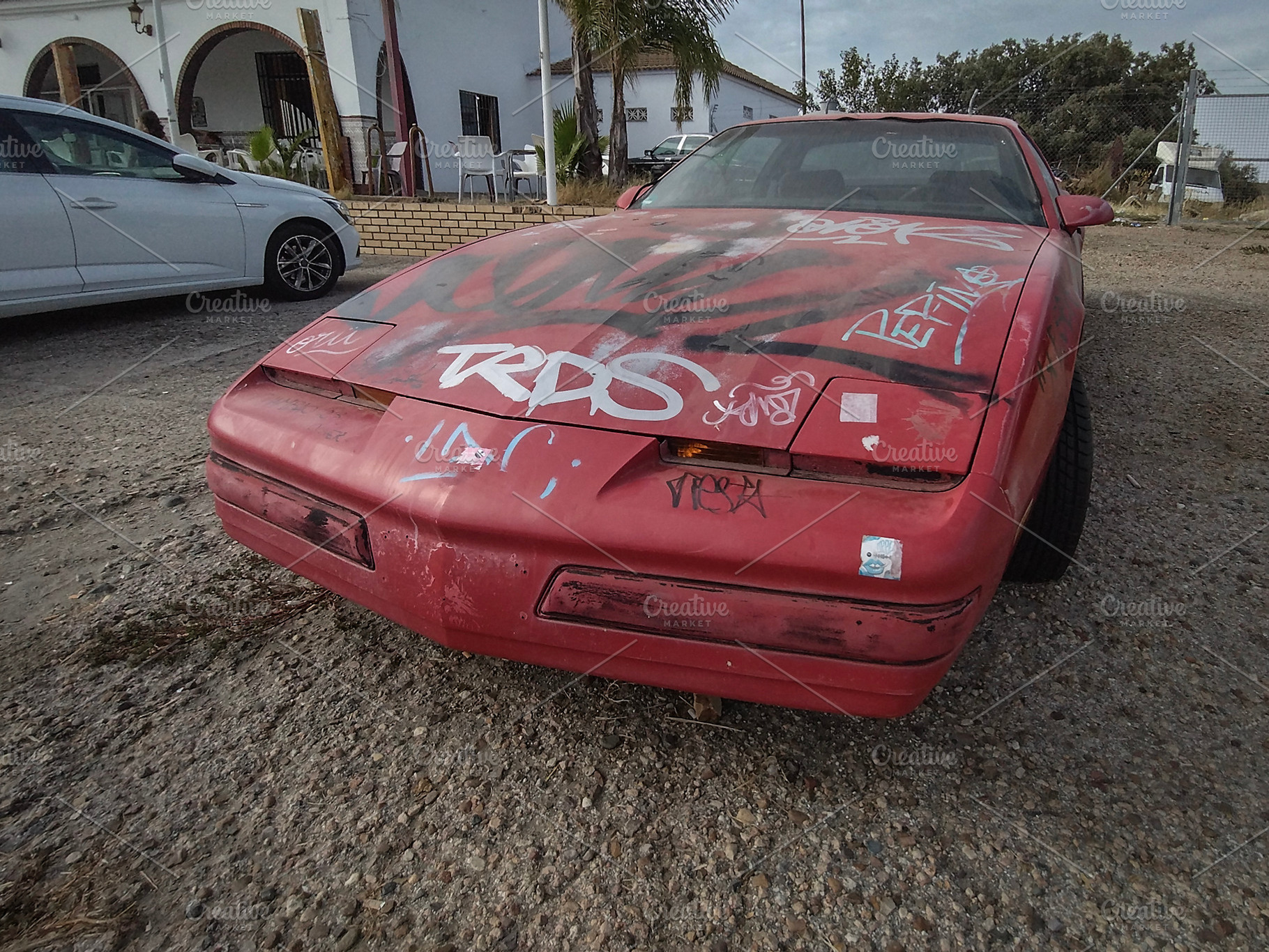 Graffitied red sports car on gravel in urban setting, a Transportation Photo by DanFLCreativo