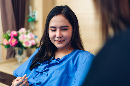 Portrait of smiling asian woman patient sitting on bed looking a, a Person Photo by Art_Photo