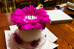 White cake adorned with vibrant pink feathers in decorative presentation, a Photo by AS photostudio