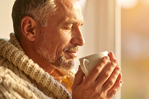 Middle-aged man with eyes closed, holding a warm cup with both h, a Health & Medical Photo by DanFLCreativo