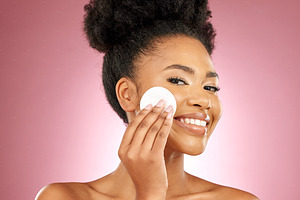 Black woman, cotton pad and skincare with makeup, portrait and facial on a studio background. Female person, face and happy model with cosmetics, aesthetic and cleaning with patches, shine and glow, a Photo by Peopleimages.com
