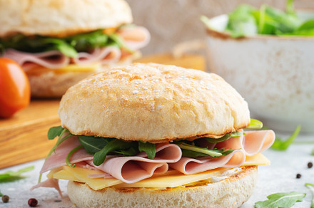 Two homemade sandwiches with ham, cheese and arugula on a concrete table., a Food & Drink Photo by Budarinphoto