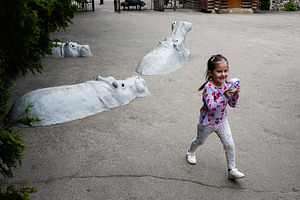 Girl joyfully playing near creative hippo sculptures in a public park setting, a Photo by AS photostudio