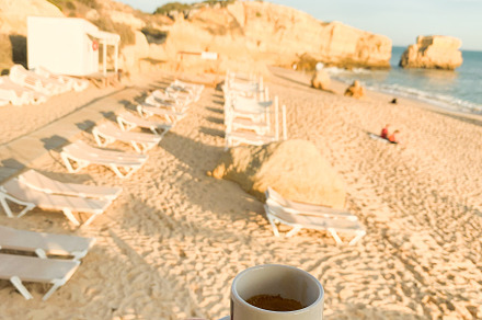 Hand holding coffee cup against the backdrop of a golden sandy b