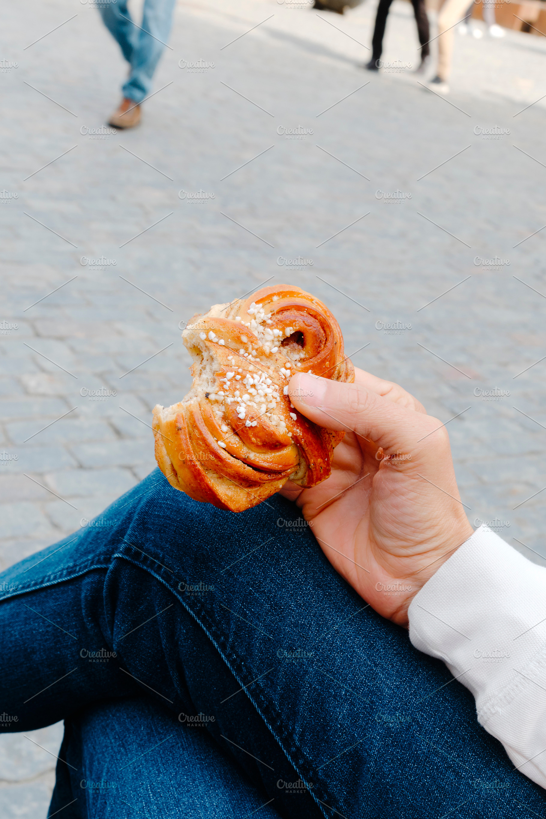 a man holds a bitten kanelbulle in a public square, a Photo by Nito