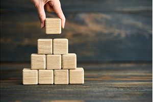Hand placing last wooden cube on, a Business Photo by Gladkov photography
