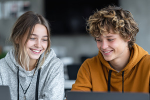 Two smiling teens using laptops toge, a Photo by Pixeness Studio