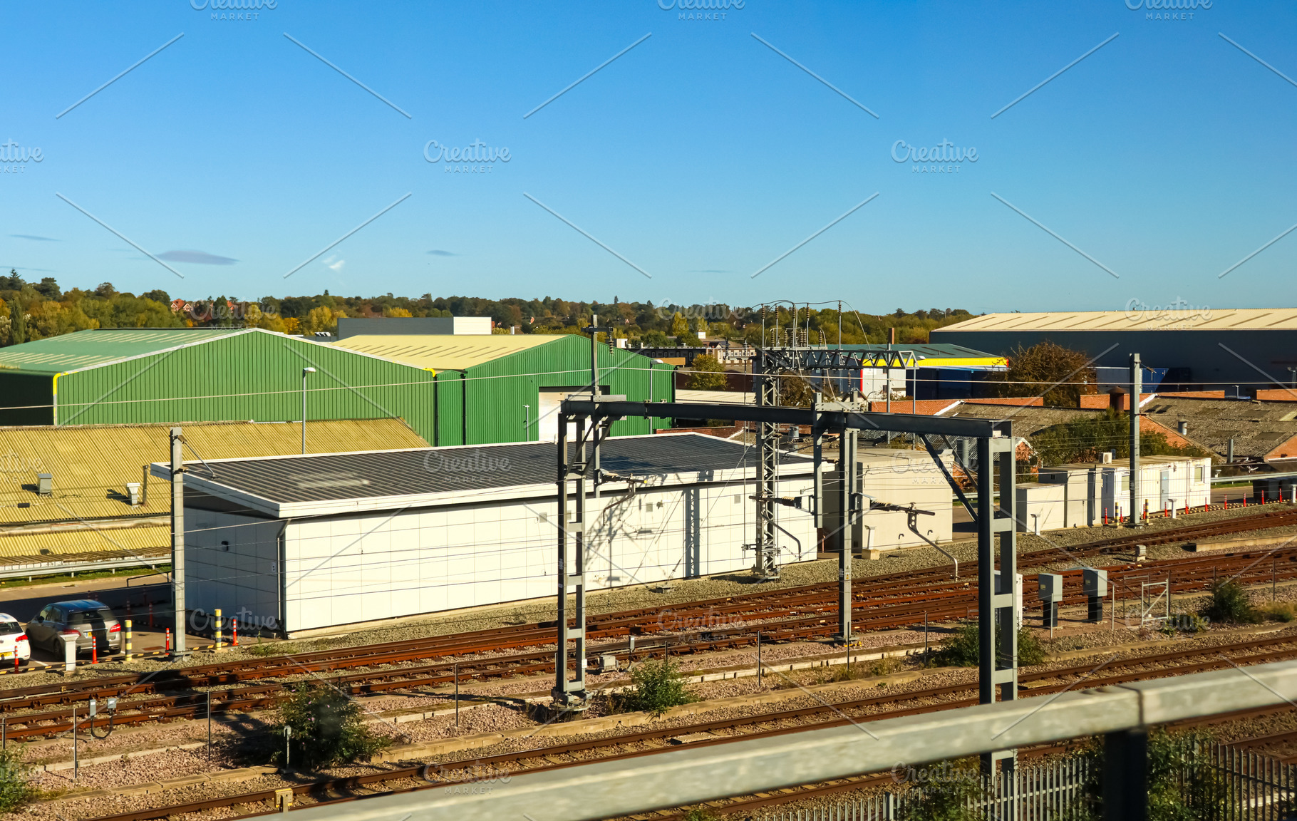 Railway tracks passing industrial warehouses under a sunny blue sky, urban tran, a Photo by Studio ANNA