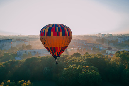 Colorful hot air balloon takes off from green park in small european city at su