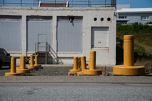 Industrial building exterior with yellow barriers in Akranes, Iceland under sun, a Photo by AS photostudio