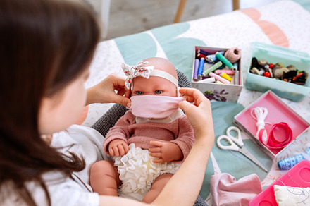Girl trying on her doll a mask that she is sewing, a Person Photo by davidpereiras