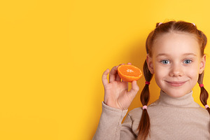 Cheerful young girl holding an orange slice against a vibrant ye, a Photo by Ales Munt