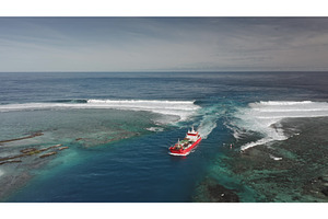 Red cargo ship sailing near a coral, a Transportation Photo by Goinyk