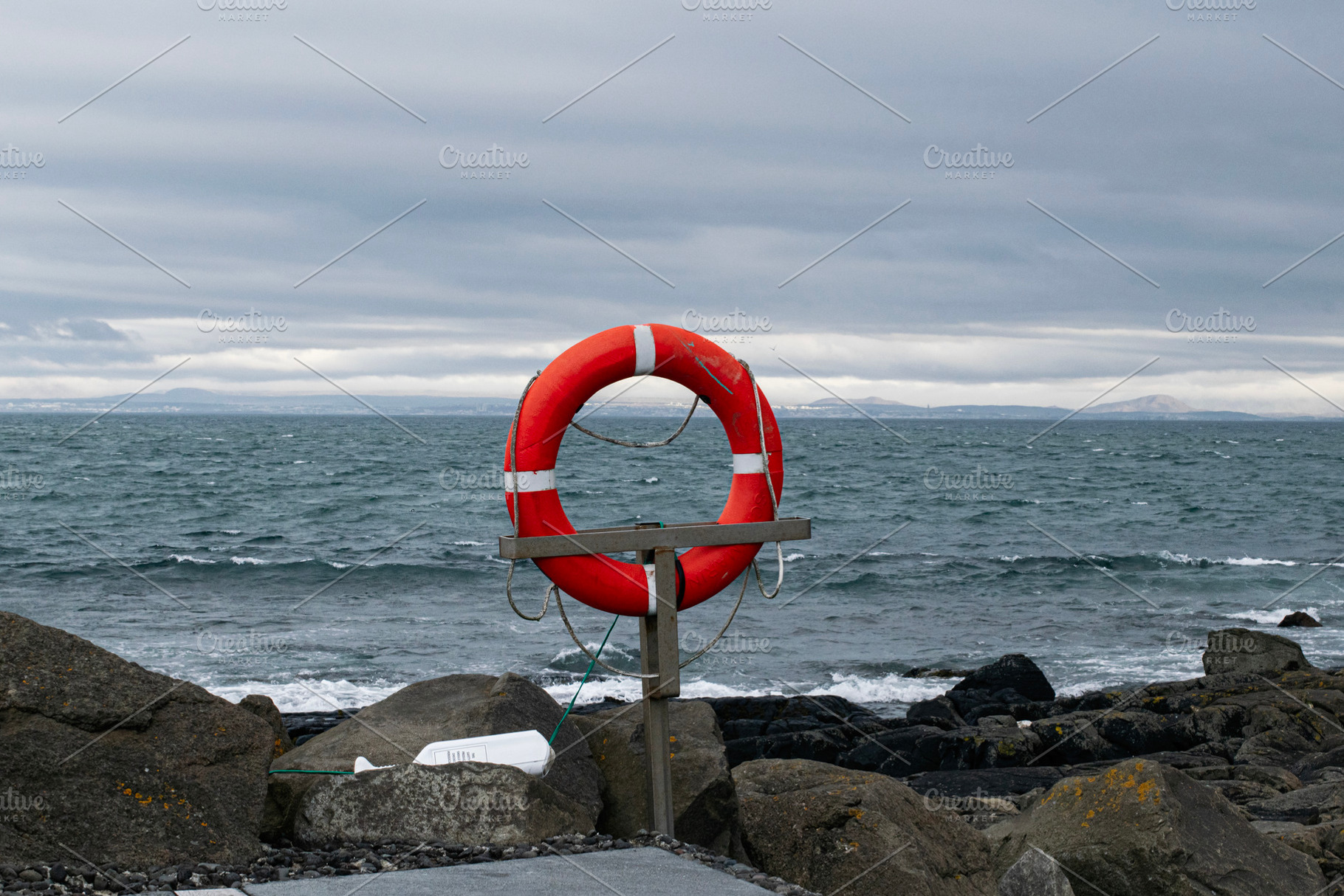 Lifesaver on a rock-lined coast in Akranes, Iceland under a cloudy sky, a Photo by AS photostudio