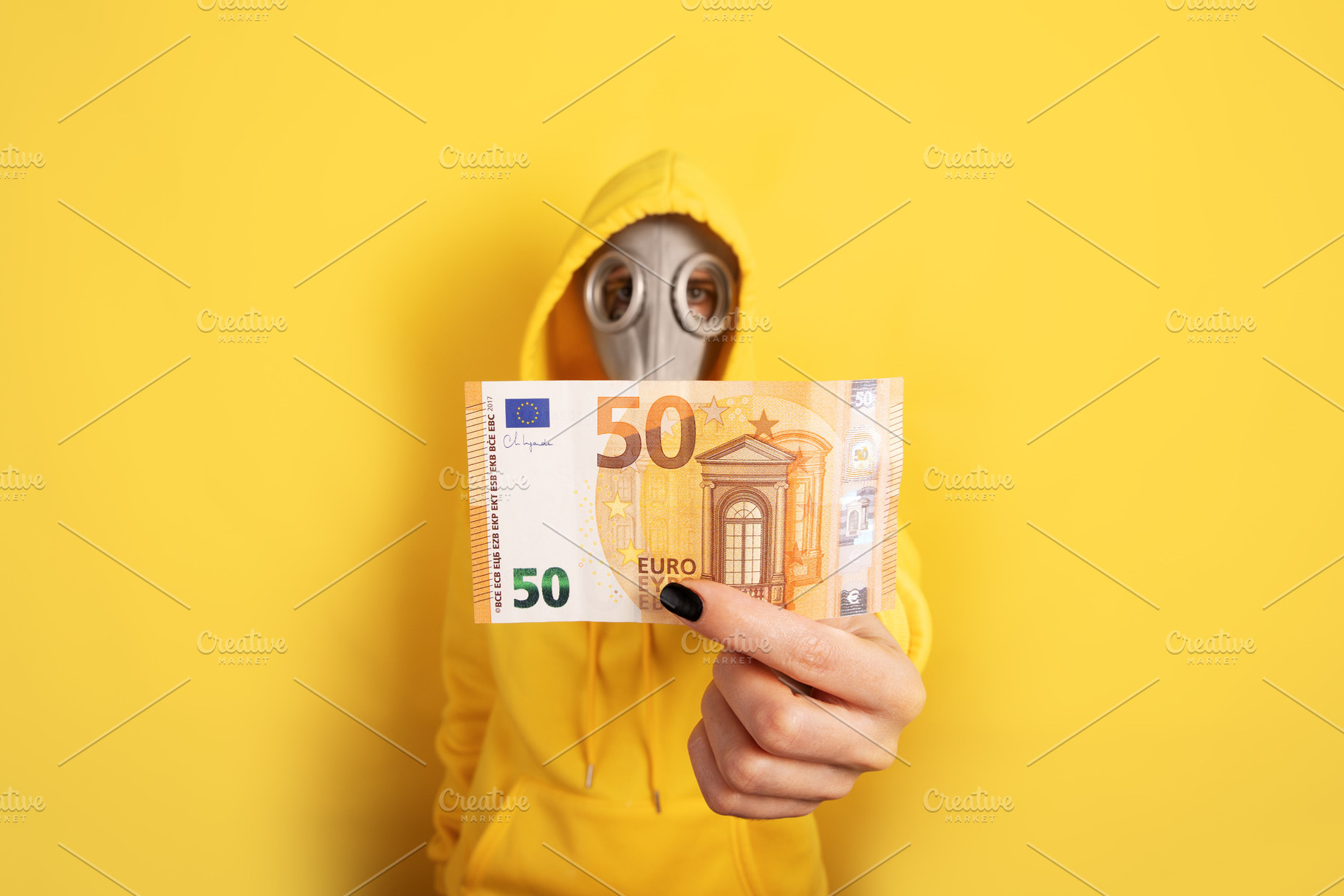 Individual in yellow hoodie and gas mask holding 50 euro banknot, a Person Photo by Ales Munt
