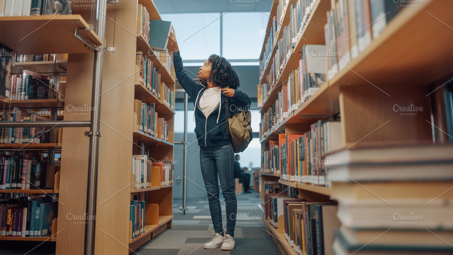 Black teenage student with curly hair reaching for a book on an, a School & Education Photo by DanFLCreativo