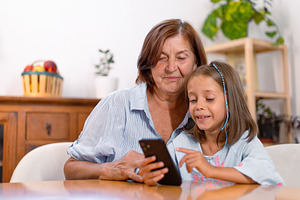 Granddaughter and grandmother using smartphone together at home, a Photo by andreonegin market