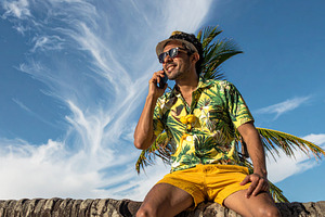 A young man sitting on palm tree using a mobile phone, a Person Photo by DanFLCreativo