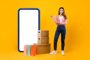 Woman Standing Near Big Phone And Cardboard Boxes, Yellow Background, a Photo by Prostock-Studio