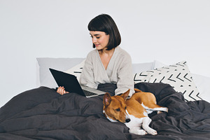 Girl works remotely from bed featuring woman, dog, and face