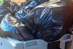 Overflowing dumpster with black garbage bags near brick wall, an Industrial Photo by Antonio Gravante Market