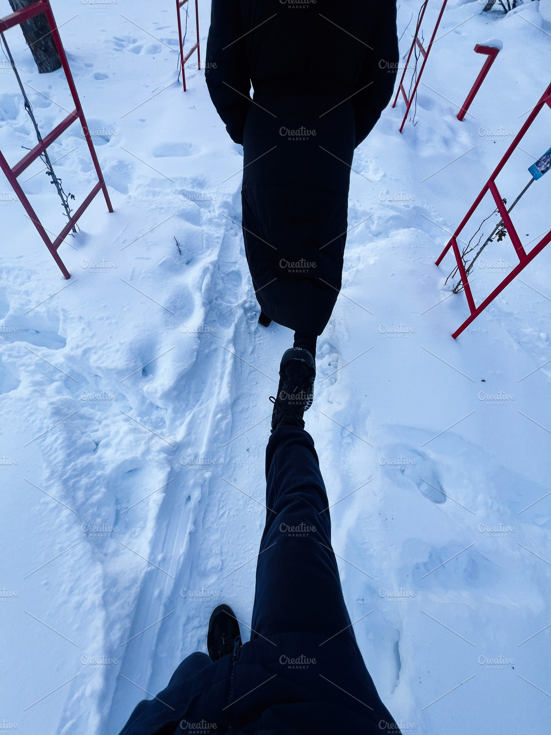 Two people walk through a snowy path between red rails in a winter scene, a Photo by AS photostudio