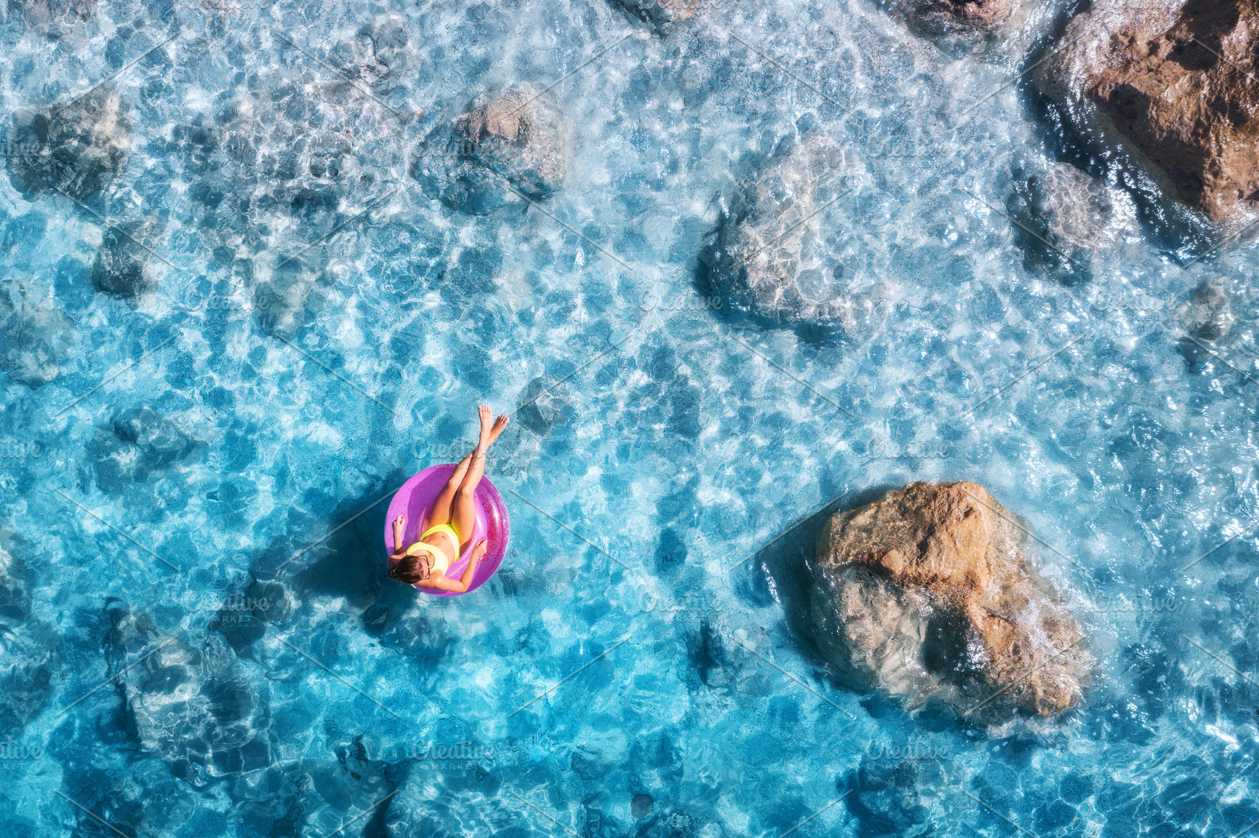 Aerial view of a young woman swimming with swim ring in blue sea, a Holiday Photo by den-belitsky