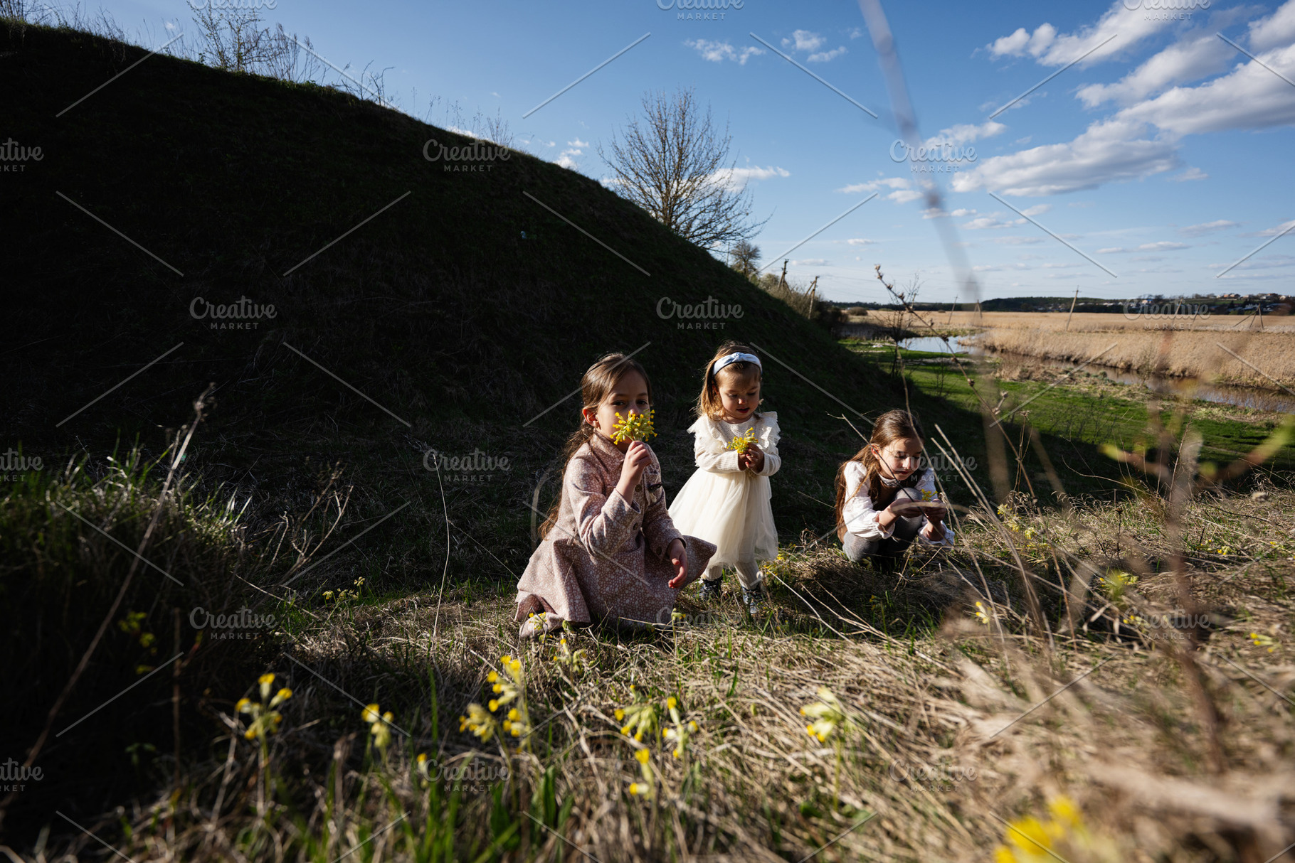 Three young girls picking wildflowers in a sunny spring meadow near a river, pl, a Person Photo by AS photostudio