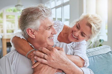 Love, happy and senior couple hug and bonding on sofa, smile and relax in home together. Retirement, freedom and happy man and woman sharing a romantic embrace, enjoying conversation and relationship, a Photo by Peopleimages.com