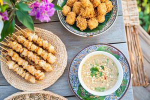 Satay skewers and shrimp with rice, sauces, and orchids arranged, a Photo by Dvoevnore photos
