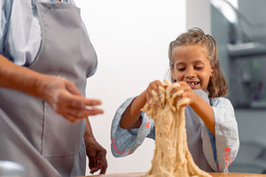 Happy girl kneading dough while baking with grandmother at home, a Photo by andreonegin market