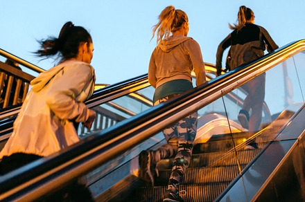 Women friends training running up escalator in city on sunset