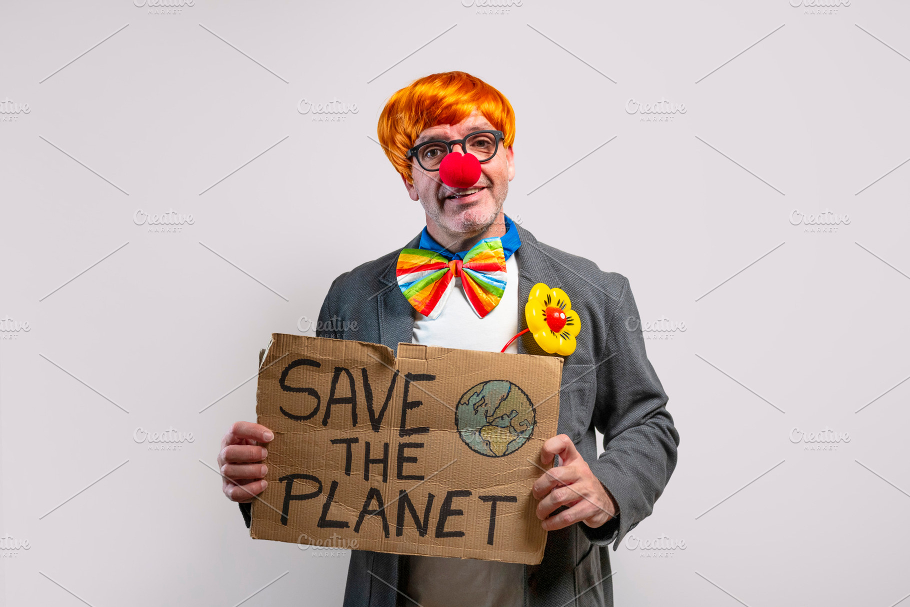 Clown with red nose and orange wig holding up a save the planet sign, a Person Photo by karrastock