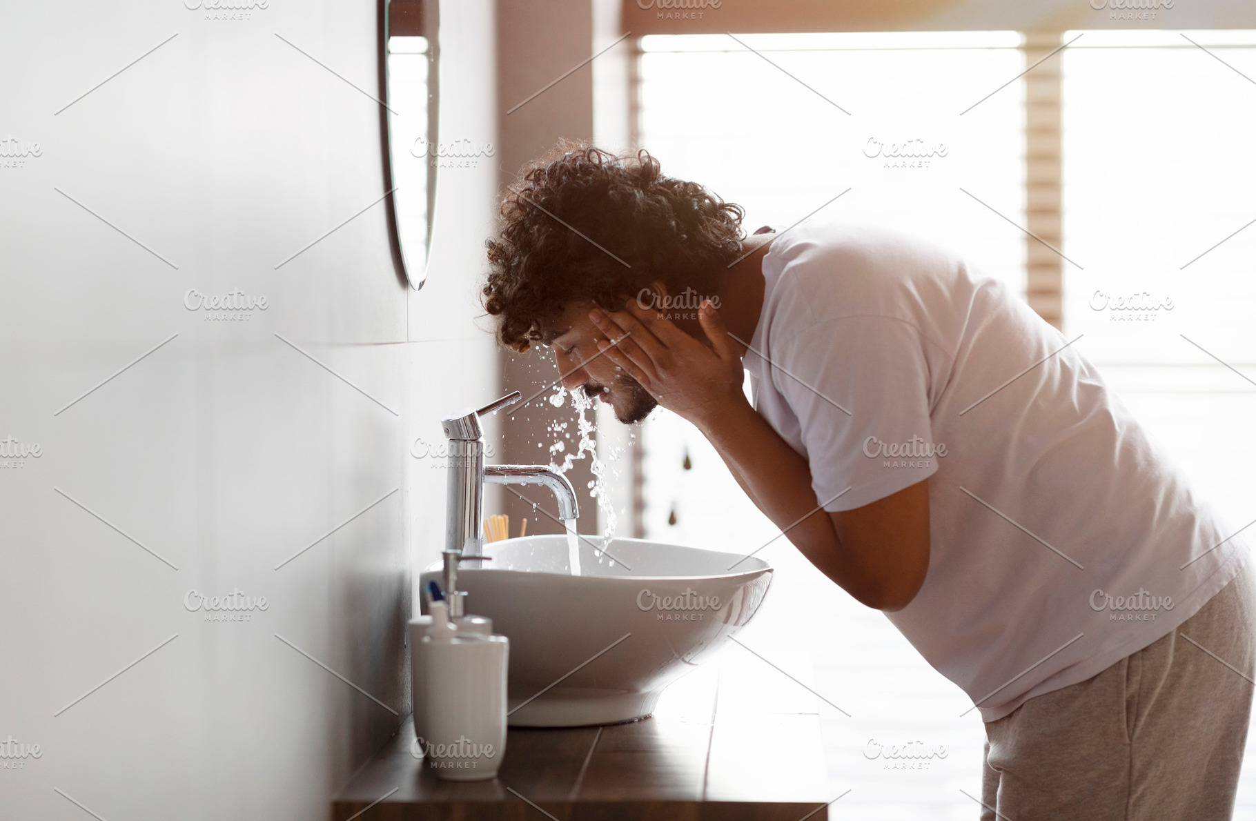 Young indian man washing face with clear water from tap bending over sink, doin, a Person Photo by Prostock-Studio