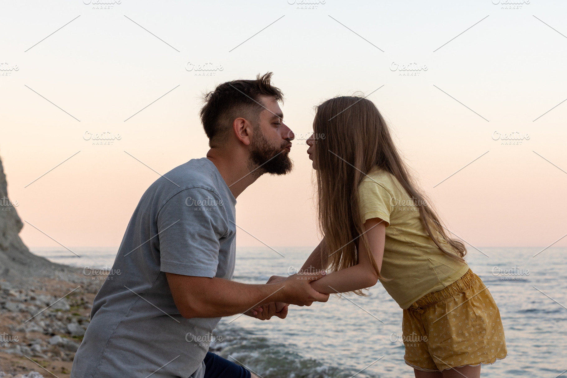 Man and young girl hold hands, sharing a tender moment by the seaside at sunset, a Person Photo by Ales Munt