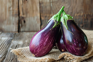 Fresh eggplants with sackcloth on wooden table, a Food & Drink Photo by AlyaAnd