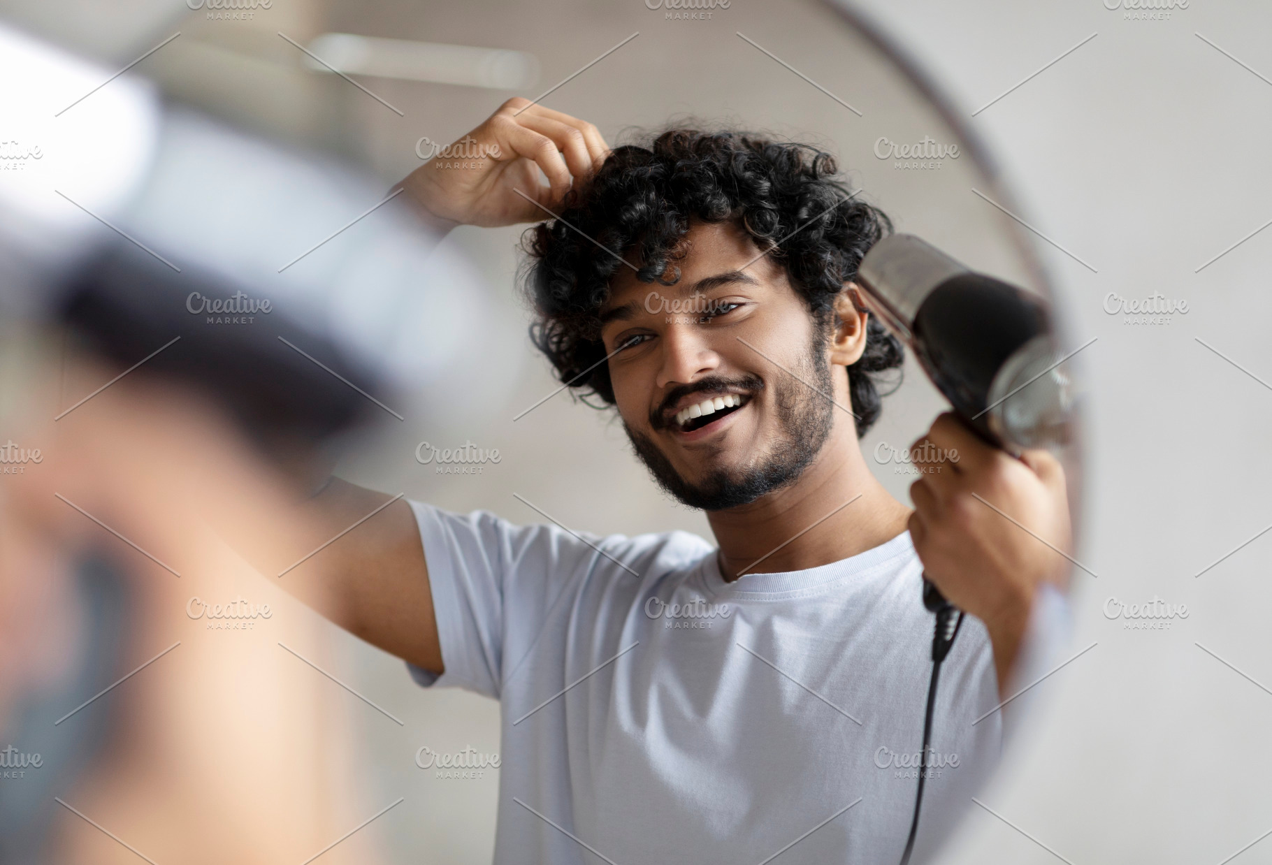 Excited indian man using hairdryer after shower, drying his curly hair, making, a Person Photo by Prostock-Studio