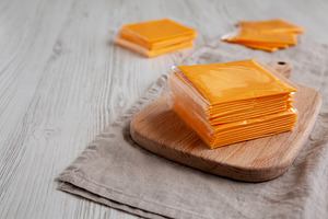 Stack of American Cheese Slices in Wrappers, side view., a Food & Drink Photo by LiudmylaChuhunova