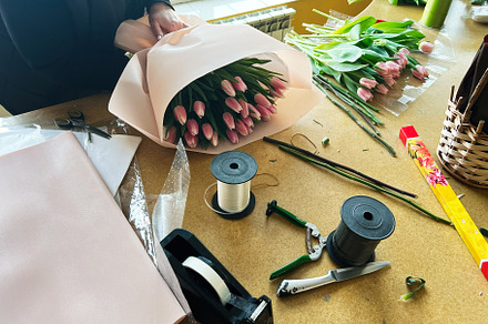 Person arranging pink tulip bouquet surrounded by floral decorations and materi, a Photo by AS photostudio