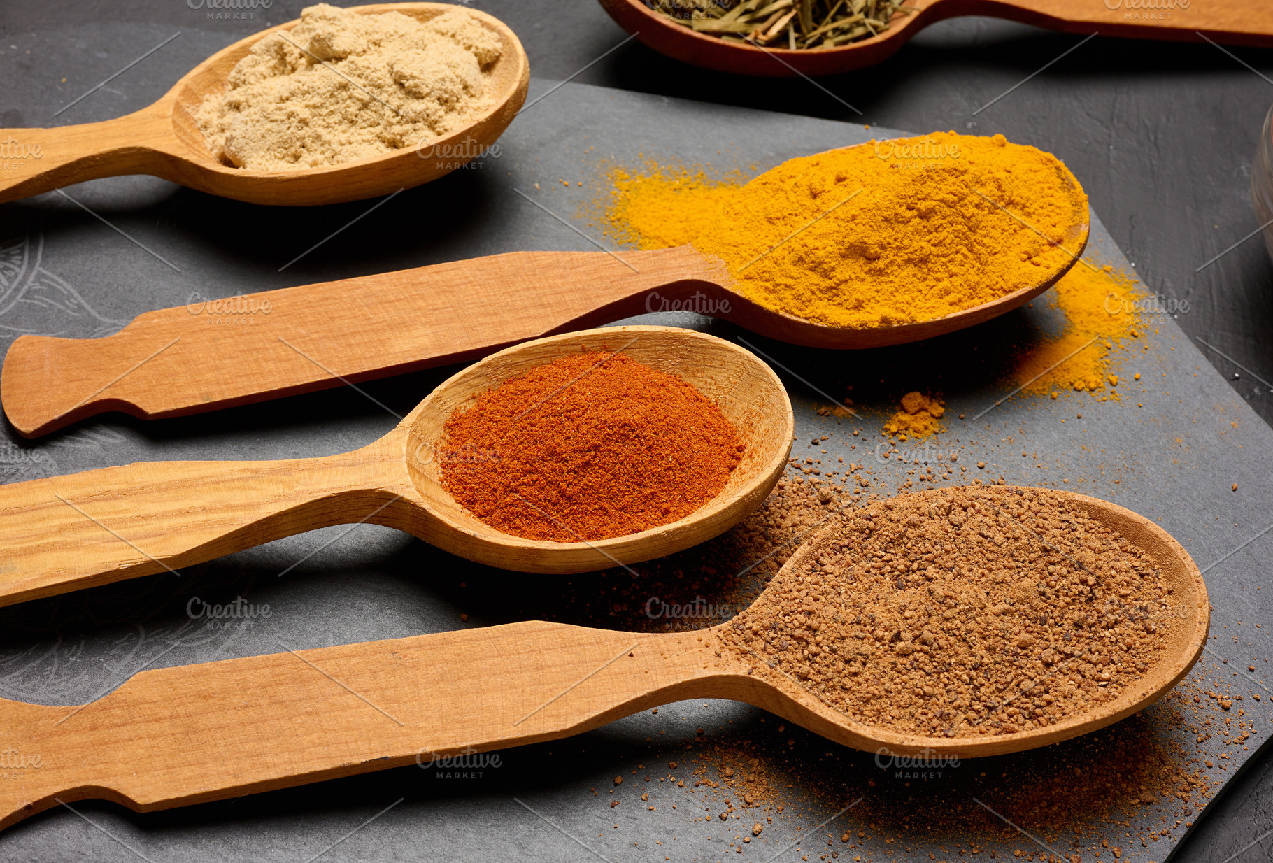 Assorted ground spices in wooden spoons, turmeric, paprika, nutm, a Food & Drink Photo by ndanko