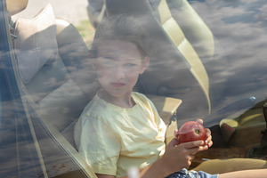 Young girl sitting inside a car, holding an apple, seen through a window with r, a Person Photo by Ales Munt
