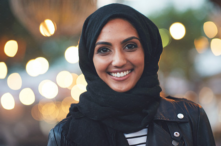 Portrait muslim woman smiling confident arab female wearing hijab headscarf in city evening with lights in background, a Photo by Peopleimages.com