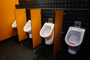 Modern public restroom with orange walls and white ceramic urinals separated by, a Photo by AS photostudio